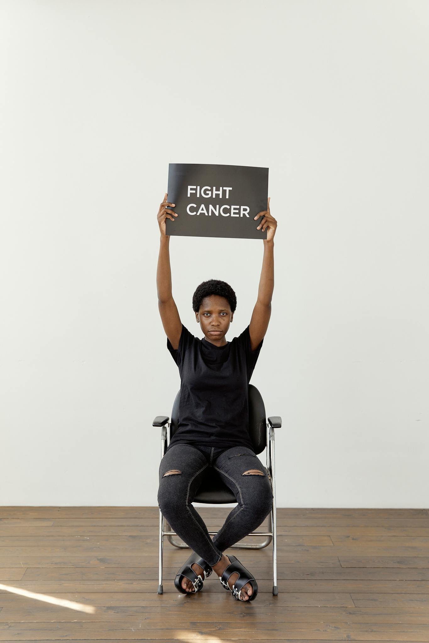 Black woman holding sign to raise cancer awareness indoors.