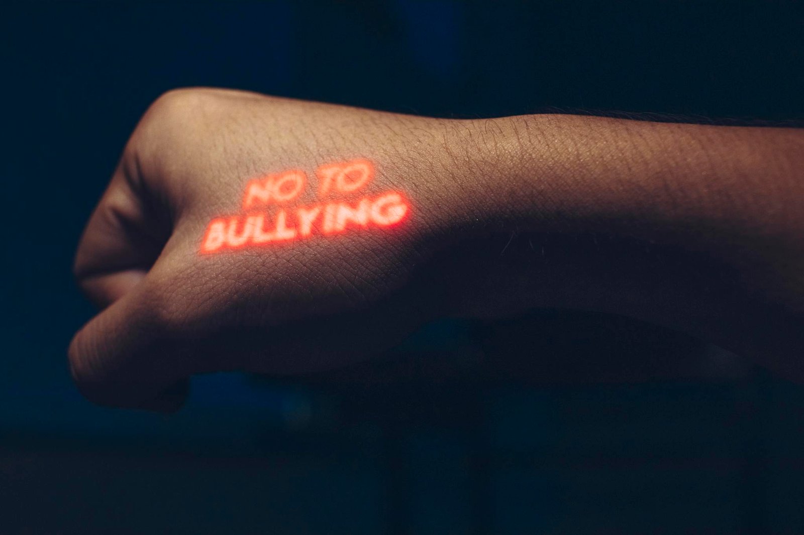 Close-up of a hand with a projected anti-bullying message in a dark setting.